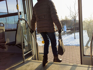 Woman passenger with jeans and coat jacket with hand bag getting off the bus during winters. Female...