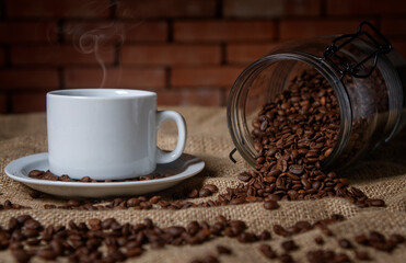 cup of coffee and a glass jar with coffee beans scattered on the table.