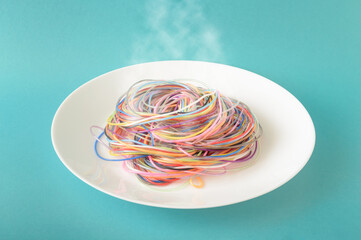 Colored cables on a plate from which steam comes out on a blue background. A concept inspired by spaghetti and food. Minimal photography style.
