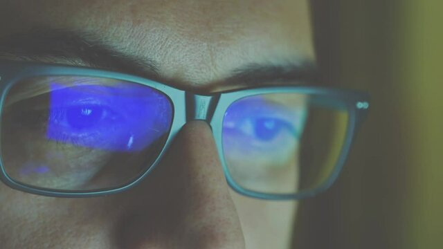 Close up portrait of a software engineer who is working: the eyes are focused on the screen, on the lens of the glasses we see the reflection. Vintage cine effect.