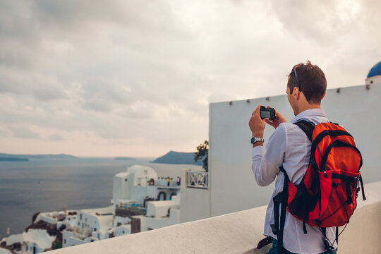 Santorini tourist man taking photo of Caldera in sea from Oia, Greece on camera. Backpacker travels during summer