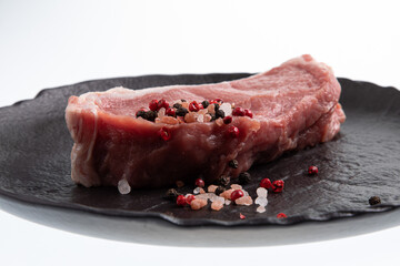 Sliced raw calf meat with a thin layer of fat around it, pink and black peppercorn and sea salt plated on black handmade ceramic plate