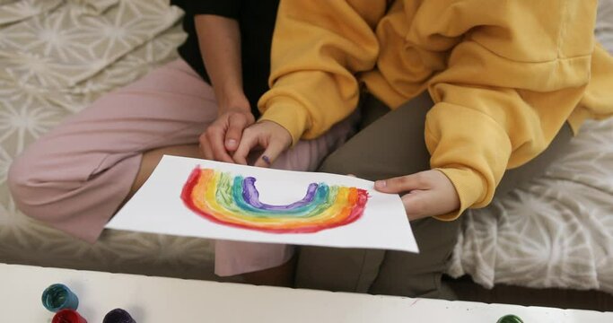 LGBT couple of girls sitting on the couch gently holding hands demonstrating freedom independence and love take in their hands a picture of a rainbow LGBT flag