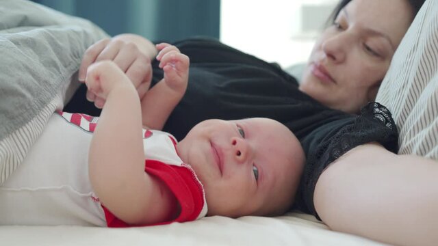 Mother and baby lying in bed together, 1.5 month old baby boy, kid and mom bonding, co-sleeping and bed sharing with babies. High quality 4k footage