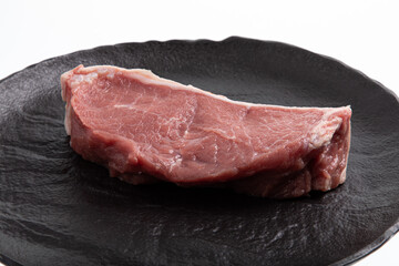 Sliced raw calf meat on black handmade plate isolated on white