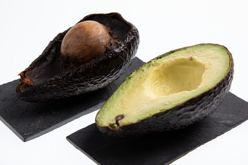 Fresh and ripe avocado next to rotting avocado cut in half with seed visible isolated on white