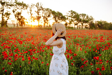 Photo of a girl in a white dress on a sunset background. Woman in a ripe field of poppies....