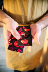 hands of a pastry chef who breaks a bar of chocolate with strawberries in a brown apron in the kitchen. High quality photo