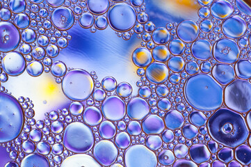 Abstract texture formed by drops of oil and water, backlit in blue, yellow and purple colors