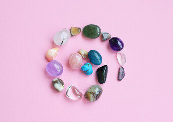 The circle is lined with natural minerals. Semi-precious stones of different colors, raw and processed. Amethyst, rose quartz, agate, apatite, aventurine on a pink background.