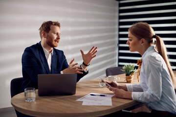 Businessman talking to female coworker while using laptop during a  meeting in the office.