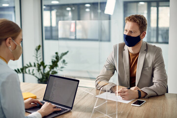 Fototapeta na wymiar Businessman with face mask communicating with colleague through protective glass due to coronavirus pandemic.