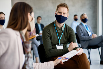 Entrepreneur communicating with female colleague while attending business seminar in board room during coronavirus pandemic.