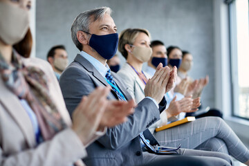 Large group of entrepreneurs wearing face masks and applauding after successful seminar in board...