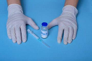 Obraz na płótnie Canvas Medical concept. On a blue background doctor's hands in white gloves, coronavirus vaccine, syringe. virus protection.Concept: prevention of coronavirus