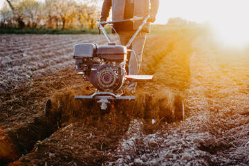 work with a walk-behind tractor in the field of a home farm, plow the soil for sowing. - obrazy, fototapety, plakaty