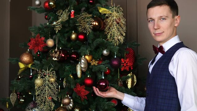 Portrait of handsome man standing near christmas tree and showing christmas toy