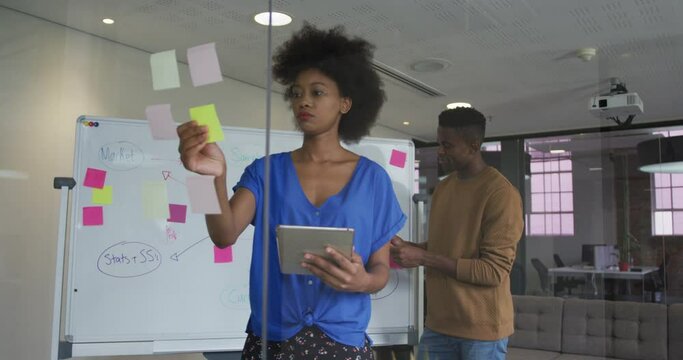 African american male and female business colleagues brainstorming in meeting room using glass wall