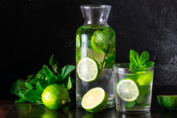 Detox refreshing drink with ice, lime and aromatic mint leaves on dark background. 