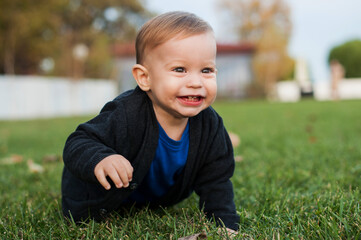Beautiful and happy baby boy playing on the green grass in the park. Childhood.