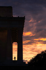 A tourist silhouetted against the fiery sunset sky at the Lincoln Memorial in Washington DC.