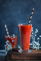  Two glasses with fresh tomato juice and drinking straws on old wooden board on dark rustic background