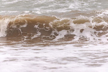 Wave with raised sand from the bottom. Wave close-up. A wave breaking on the shore.