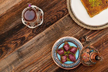 Closeup of traditional Turkish desserts: violet baklava and Kadayif with pistachio powder (Burma kadayif) with Turkish tea on wooden background. Most popular in Ramadan time (Turkish: Ramazan bayrami)