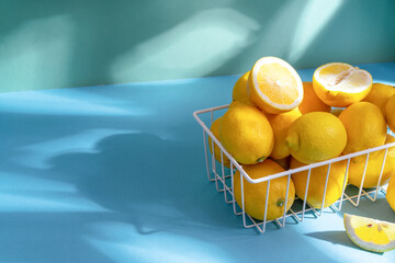 Yellow lemons in white basket on simple background, light through the foliage, the concept of spring vitamin deficiency and healthy lifestyle.