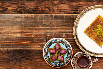 Closeup of traditional Turkish desserts: violet baklava and Kadayif with pistachio powder (Burma kadayif) with Turkish tea on wooden background. Most popular in Ramadan time (Turkish: Ramazan bayrami)