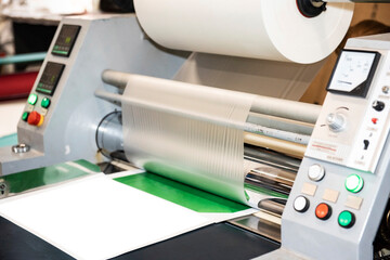 The industrial laminator applies the film to the paper in the production room of the printing house - obrazy, fototapety, plakaty