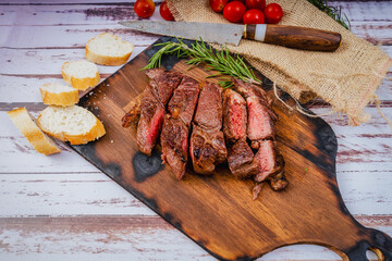 Churrasco of meat cut into pieces on a wooden board in a rustic setting. 45 degree view.