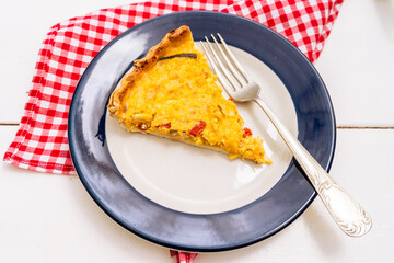 Exquisite portion of homemade corn cake or quiche with onion, red bell pepper and chives on a white plate with a blue rim. Healthy and natural food.