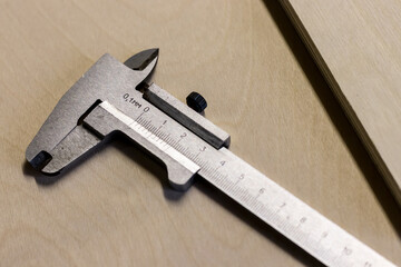 Old mechanical metal vernier caliper lies on a wooden table, next to a sheet of plywood