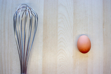 Wire whisk and egg on wood background