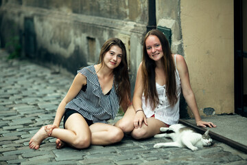Fototapeta na wymiar Two teenage girls friends sitting on the pavement with a cat.