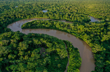 Aerial view of a tropical river meandering through a tropical forest with a canoe going over the...