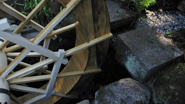 Water wheel rotates slowly with stream of water, rocks frame the water flow