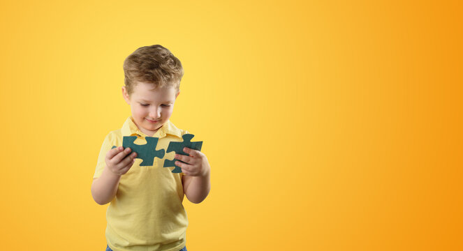 A little boy holds puzzle pieces in his hands. A game for the development of the brain, concentration. Copy space - Powered by Adobe