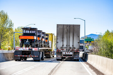 Two loaded big rig semi trucks with different semi trailers running side by side on the narrow two...