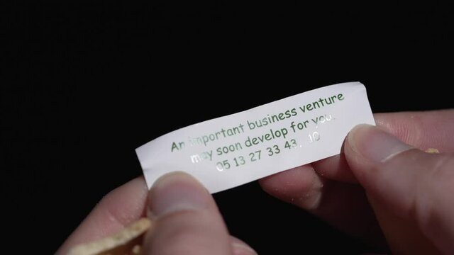 This close up, macro video shows anonymous hands opening a fortune cookie to reveal a fortune telling paper.