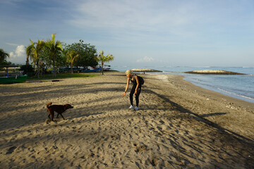 A woman walking around Kuta Beach Bali and playing with the doga.