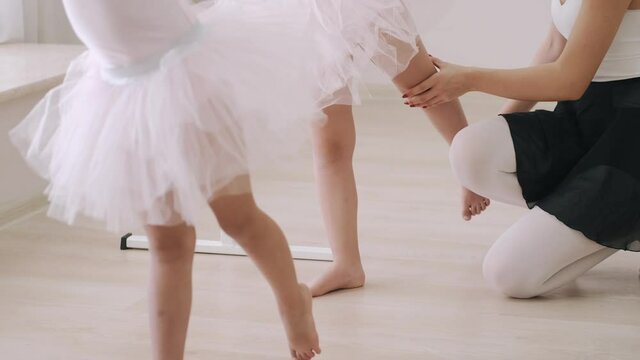 Two little girls practicing choreographic elements on ballet barre with help of teacher in dance school