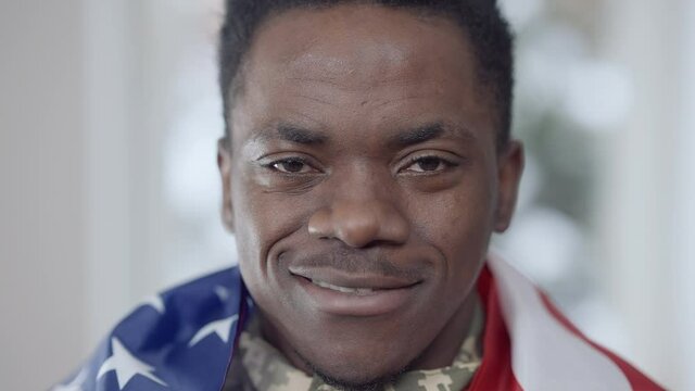 Headshot of confident brave African American soldier posing at home with USA flag. Close-up portrait of positive handsome man smiling looking at camera. Courage and patriotism concept