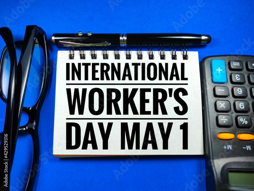 Word INTERNATIONAL WORKER'S DAY MAY 1 on blue background with calculator,pen and glasses.Labour day concept.