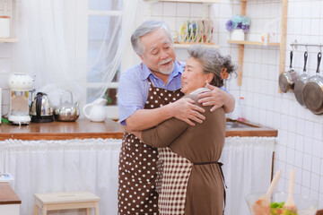 Asian happy retired senior smiling cute eldery couple hugging & holding hands together in kitchen at home Romantic relationship of lovely & beautiful marriage lover with happiness retirement lifestyle