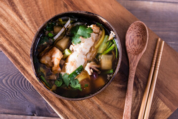 Asian soup with halibut and seafood (hemultan) shrimps, mussels and young octopus. Korean traditional soup on a dark wooden background with herbs. Wooden plate and spoon.