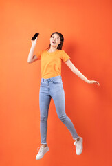 Fototapeta na wymiar Young Asian woman wearing orange T-shirt jumping on orange background