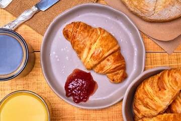 continental breakfast, a french croissant with strawberry jam, a glass of orange juice and a cup of coffee, with loaves of bread in the background on a wooden table. rustic concept. IN TOP VIEW