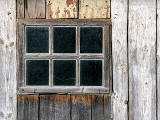 weathered wooden barn wall. old window frame with dirty glass.